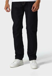 Temno modri kavbojki z ravnim krojem, kontrastnim šivanjem in sprednjimi žepi, v kombinaciji z belimi športnimi čevlji.