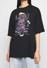 Černé oversized tričko s barevným grafickým potiskem draka, doplněné květinovými vzory a siluetou hor. Krátké rukávy a kulatý výstřih.