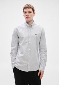 Πουκάμισο με κουμπιά μπροστά, με κάθετες γκρι και λευκές ρίγες, με γιακά, μακριά μανίκια και μικρό μαύρο λογότυπο στο στήθος. Βαμβακερό υλικό.