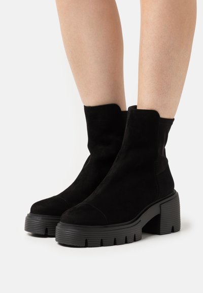Cizme negre până la glezne, din suede, cu o finisare netedă, având o talpă groasă cu nervuri și un design cu vârf rotunjit.