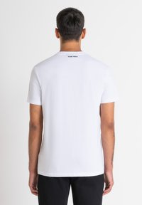 Camiseta corta de manga blanca hecha de algodón, con cuello redondo y un pequeño logo negro en la parte posterior cerca del cuello.