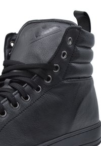 Czarne sneakersy typu high-top wykonane z teksturowanej skóry, z metalowymi oczkami, płaskimi sznurowadłami i wyściełanym kołnierzem. Gładka gumowa podeszwa.