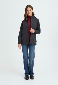 Svart lett jakke med glidelås foran, romslig hette og elastiske mansjetter, kombinert med en vinrød turtleneck og blå jeans.