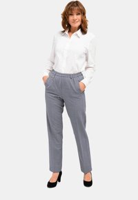 Grijze, geruite broek met een relaxte pasvorm en een elastische tailleband. Gecombineerd met een wit overhemd met knopen en zwarte hoge hakken.