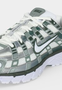 Λευκό και γκρι sneaker Nike Air Zoom Spiridon Cage 2 με λευκά κορδόνια, διχτυωτό επάνω μέρος και λογότυπο Nike Swoosh σε λευκό χρώμα με μαύρο περίγραμμα.