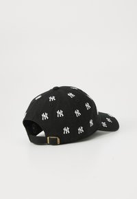 Zwarte pet met witte New York Yankees-logo's verspreid over de stof, voorzien van een verstelbare band aan de achterkant.