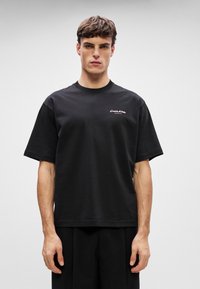 T-shirt de algodão preto de manga curta com um corte solto, apresentando um pequeno logótipo bordado branco no peito e um decote redondo.