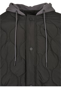 Veste matelassée noire avec capuche grise, cordons apparents et trois boutons-pression noirs à la fermeture avant.