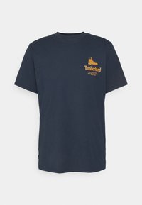 Námořnická modrá bavlněná tričko s žlutým logem Timberland a grafikou boty na levé části hrudníku. Krátké rukávy a design s kulatým výstřihem.