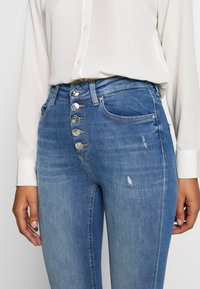 Jeans de cintura alta en azul hechos de denim, con un cierre de cinco botones, que presentan un acabado desgastado y dos bolsillos laterales.