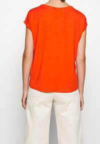 T-shirt court orange vif à manches courtes avec une coupe décontractée et un col rond. Texture douce, détails de couture minimalistes, porté avec un pantalon large beige clair.