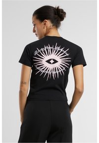 Mustast kärbitud t-särk, millel on suur roosa silma graafika päikesekiirte mustriga seljal. Lühikesed varrukad ja puuvillane materjal.