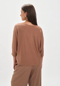 Brązowa, lekka bluzka z trzema ćwierć rękawami o luźnym kroju, charakteryzująca się miękką fakturą i okrągłym dekoltem. Styl casualowy.