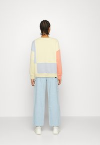 Sweter w pastelowych łatach w kolorach żółtym, niebieskim i koralowym. Posiada okrągły dekolt, długie rękawy i ściągacze na mankietach. Połączony z jasnoniebieskimi spodniami o szerokich nogawkach.