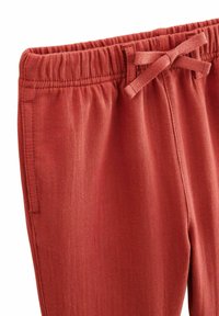 Pantalons rouges côtelés avec une taille élastique et un détail de nœud lié. Comprend des poches latérales et une texture douce. Convient pour une tenue décontractée.