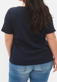 Top corto a righe blu navy con scollo a barca, abbinato a jeans denim azzurri. Texture morbida, vestibilità casual.