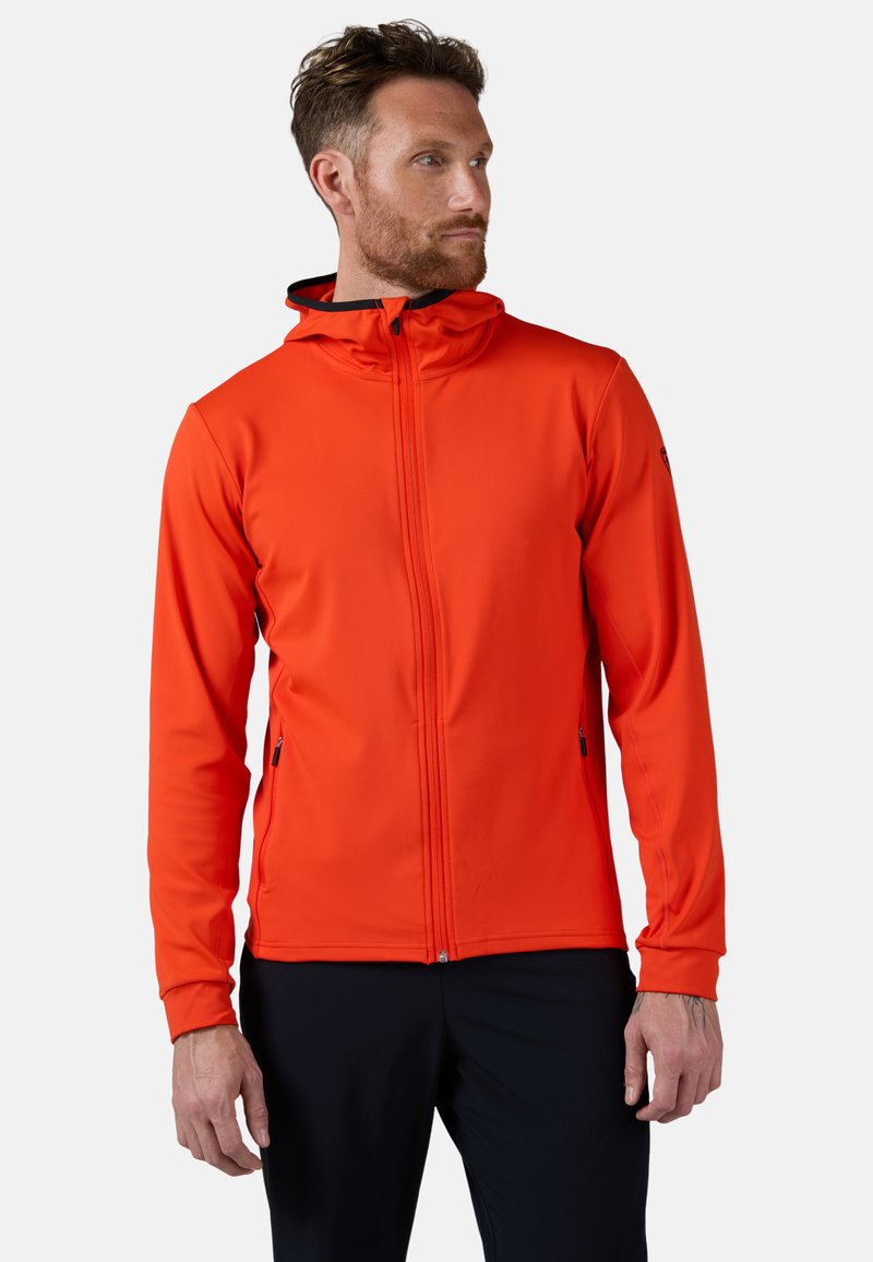 Giacca rossa con cappuccio realizzata in tessuto leggero, dotata di zip full zip, due tasche laterali e dettagli neri sul cappuccio e sui polsini.