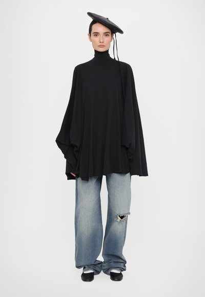 Mustapaitainen pitkähihainen paita korkean kaulan kanssa, yhdistettynä vaaleansinisiin kuluneisiin leveälahkeisiin farkkuihin ja mustiin jalkineisiin, joita korostaa musta beretti.