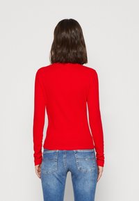 Maglietta rossa a maniche lunghe con un design aderente, texture liscia e scollatura tonda, abbinata a jeans in denim azzurro chiaro con tasche posteriori.
