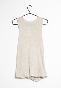 Haut beige clair sans manches en tissu texturé, avec un col rond et un ourlet asymétrique. Suspendu à un cintre métallique noir.