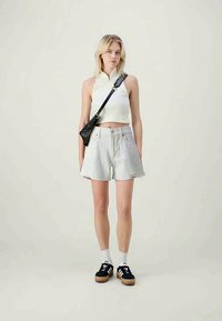 Λευκό κρουαζέ τοπ, ανοιχτό γκρι σορτσάκι με μπροστινές τσέπες, μαύρη τσάντα χιαστί και μαύρα αθλητικά παπούτσια με λευκές λεπτομέρειες. Απλό φόντο.