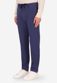 Pantaloni della tuta blu navy realizzati in tessuto morbido, con vita regolabile con cordino, gambe affusolate e tasche laterali, abbinati a sneaker bianche.