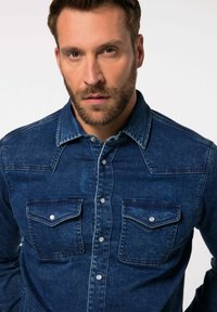 Blå denimskjorte med klassisk krave, to brystlommer og knaplukninger. Har et struktureret stof med en subtil glans.