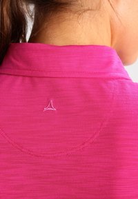 Haut de sport rose avec un tissu texturé, un col plié et un petit logo brodé au niveau de la nuque.