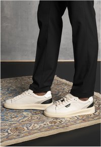 White leather sneakers with black accents and a rubber sole, featuring round laces and perforations on the toe for ventilation.