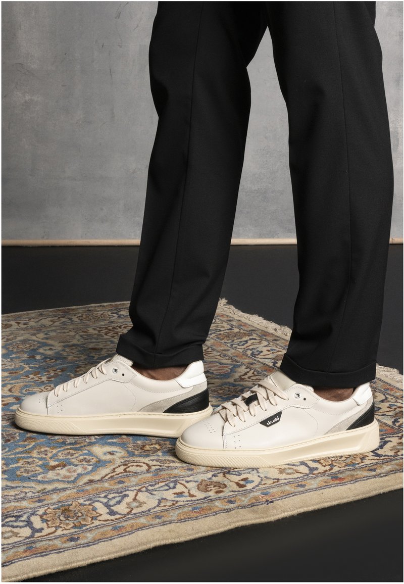 White leather sneakers with black accents and a rubber sole, featuring round laces and perforations on the toe for ventilation.