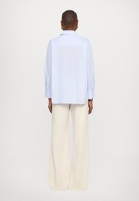 Ανοιχτό μπλέ πουκάμισο με γιακά και μακριά μανίκια, που διαθέτει ευθύ στρίφωμα. Συνδυάζεται με κρεμ παντελόνι σε φαρδιά γραμμή, προσφέροντας άνετη εφαρμογή.