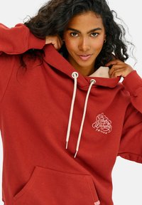 Bordový mikina vyrobená z mäkkej látky s prednou vreckom, sťahovacou šnúrkou a krémovým podšívku v kapucni. Obsahuje grafiku textu na hrudi.