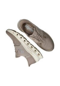 Beige Skechers Slip-Ins mit einem atmungsaktiven Mesh-Obermaterial, Schnürdetails und einer gepolsterten weißen Sohle mit Ausschnittakzenten.
