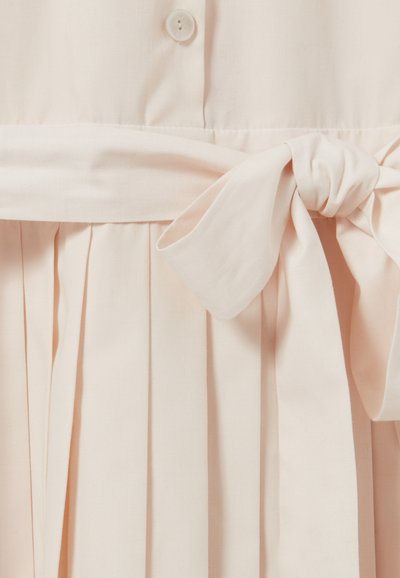 Robe rose pâle avec des plis verticaux, une ceinture à nouer à la taille et une fermeture à bouton en haut. Le tissu semble lisse et léger.