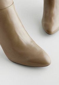 Kanga nahkkingad, millel on terav varvas ja õhuke kõrge konts, sile pind kergete kortsudega, esitades elegantset ilu.