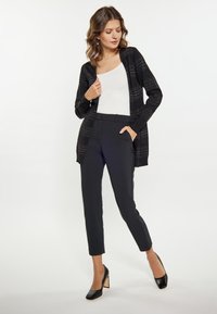 Cardigan negru din tricot cu linii orizontale subtile, purtat peste un top alb și asortat cu pantaloni negri croiți și pantofi cu toc negri.