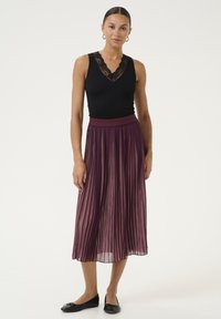 Top a fascia nera a costine con bordi in pizzo, abbinato a una gonna plissettata di lunghezza media in bordeaux. Le scarpe nere completano l'outfit.