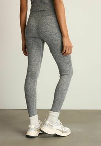 Szürke bordás leggings, texturált anyagból készült, fehér zoknikkal és vastag talpú sportcipőkkel párosítva. Magas derékszabása és testhezálló fazonja van.