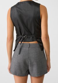 Top senza maniche nero con un motivo testurizzato, fascia in vita con accessori in metallo, abbinato a pantaloni corti grigi tagliati con un tessuto morbido.