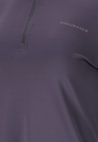 Violetti urheilupaita, jossa on puoliveto, teksturoitu kangas, jossa on hienovarainen ruudullinen kuvio, ja "ENDURANCE"-logo vaaleanharmaana.