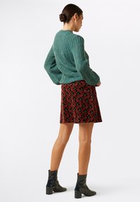 Tyrkis strikket sweater med et struktureret mønster, parret med en rød mønstret nederdel med grønne og sorte svulster, samt sorte ankelstøvler.