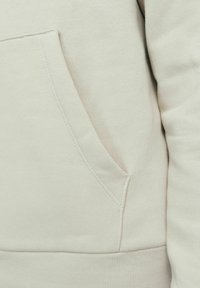 Helltaures Sweatshirt-Material mit einer Seitentasche, das eine glatte Textur und gerippte Bündchen aufweist, mit ordentlichen Nähdetails.