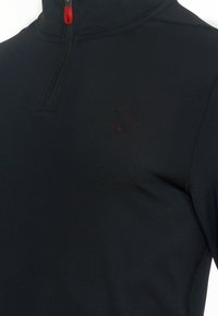 Czarna bluza z półzamkiem wykonana z lekkiego, teksturowanego materiału. Posiada czerwony suwak i dyskretny akcent w postaci logo pająka.