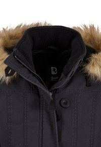 Črna jakna z umetnim krznom ob kapuci in zadrgo na ovratniku. Ima gumbe in rebraste manšete, izdelana je iz trpežnega materiala z navpičnimi šivi.