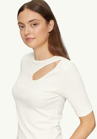 Weißes, enges T-Shirt mit einem Ausschnitt an der Schulter, aus geripptem Material. Es hat kurze Ärmel und einen runden Ausschnitt.