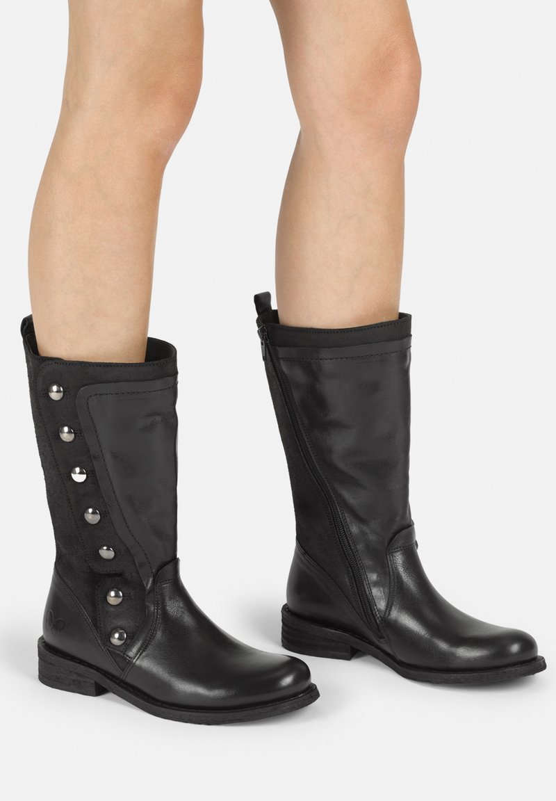 Botas de cuero negro hasta la rodilla con un cierre lateral, panel de tela y botones metálicos decorativos a lo largo del eje exterior. Suela de goma plana.