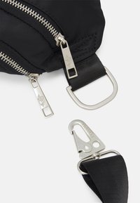 Svart nylonväska med silverfärgade dragkedjor, utrustad med metallhardware, ett brett rem och en tryckknappshake för säker fästning.