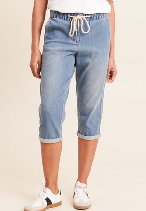 Pantalon en jean bleu clair raccourci avec taille élastique et cordon blanc, porté avec des baskets blanches et un haut blanc.