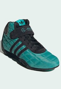 Teal quiltet sportssko med sorte detaljer, inkluderer tre sorte striber, justerbar Velcro-strop og gummisål. Har Mercedes-branding.