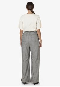 T-shirt oversized beige e pantaloni a vita alta a quadri grigi con gamba larga, dotati di fessure laterali e tasche posteriori, mostrati di spalle.